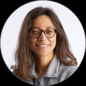 Headshot of Stephanie Argy with brown shoulder-length hair, wearing brown eyeglasses and a gray top in front of a white background