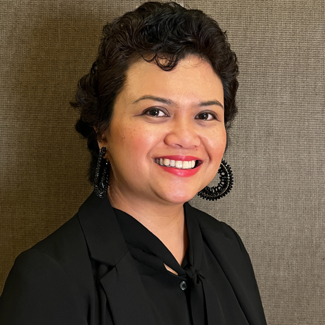 Smiling Filipinx woman with black earrings, jacket, and top.